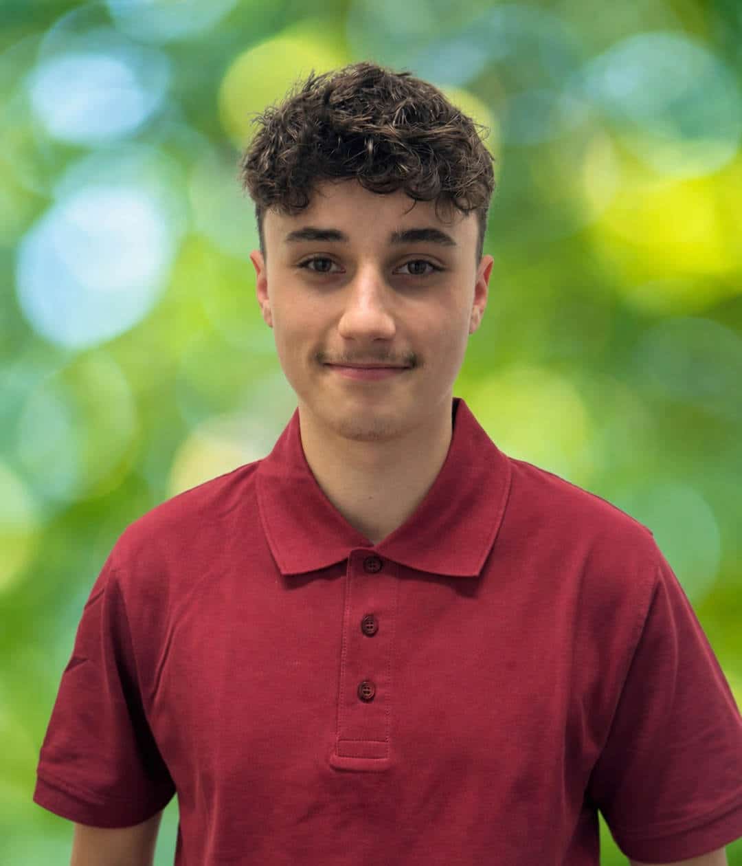 Porträt von Johannes Boeg im roten Poloshirt vor grüner Natur Porträt von Johannes Boeg mit lockigem Haar und rotem Poloshirt vor einem weich verschwommenen grünen Hintergrund