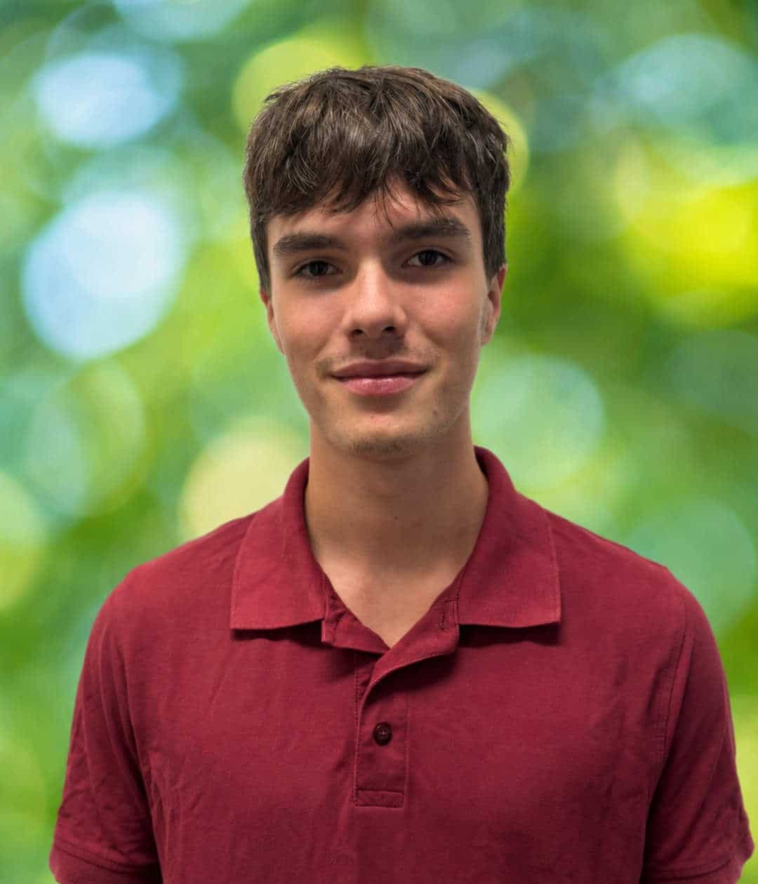 Porträt von Levi Weiberg im dunkelroten Poloshirt, grüner Hintergrund Porträt eines jungen Mannes mit dunkelbraunem Haar und dunkelrotem Poloshirt vor unscharfem grünem Hintergrund.