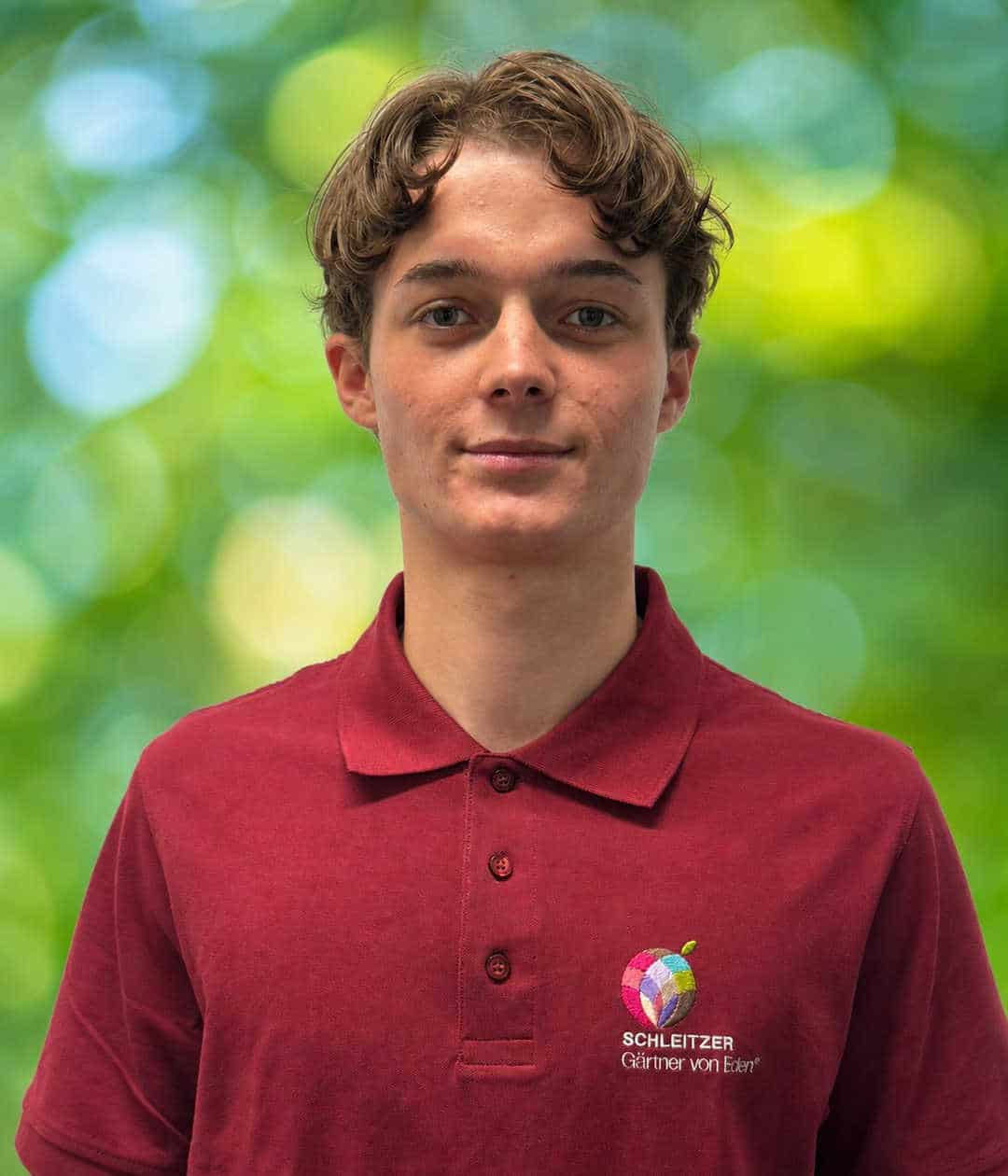 Porträt von Spike Lembert mit lockigem Haar und rotem Poloshirt samt buntem Schleitzer-Logo vor grünem Hintergrund